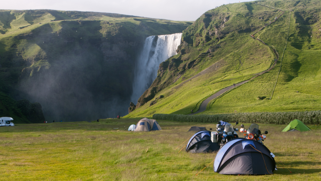 Tents pitched on some grass in front of Skógafoss Waterfall.