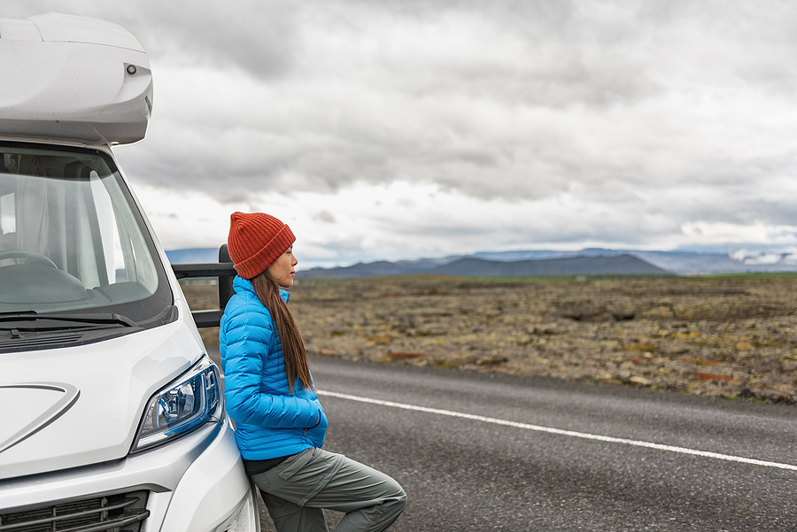 A female tourist leaning against her RV camper trailer parked on the side of a road in Iceland during an autumn trip